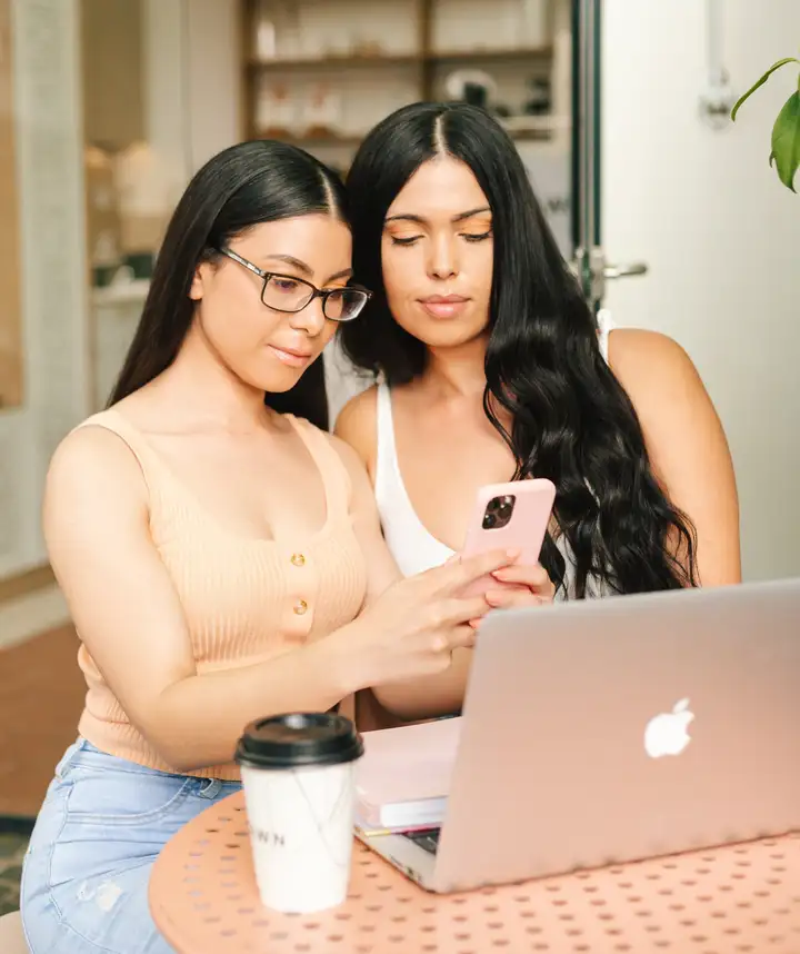 Kamara and Bianca from The Glow Up Marketing reviewing content on a phone and laptop